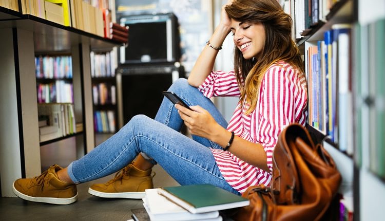 Happy student woman using phone instead of learning in library