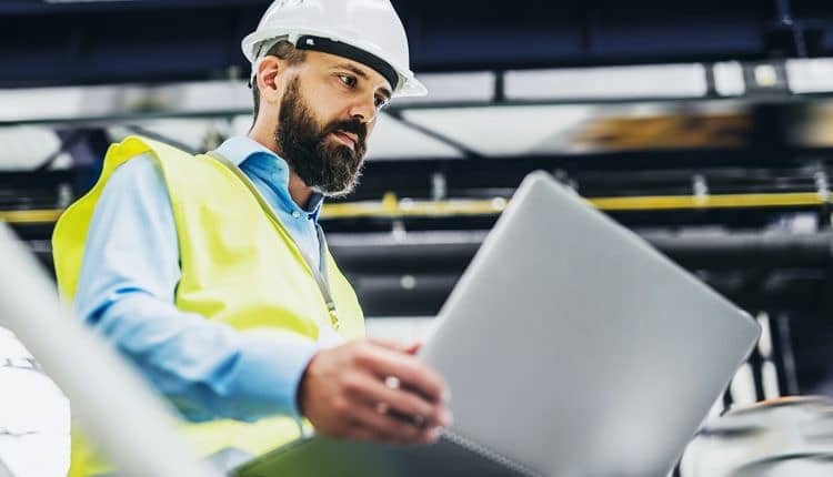 A portrait of an industrial man engineer with laptop in a factory, working.