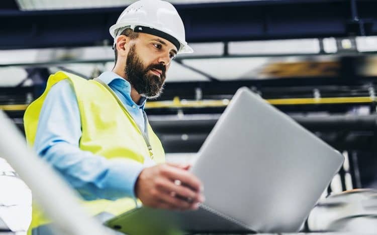 A portrait of an industrial man engineer with laptop in a factory, working.