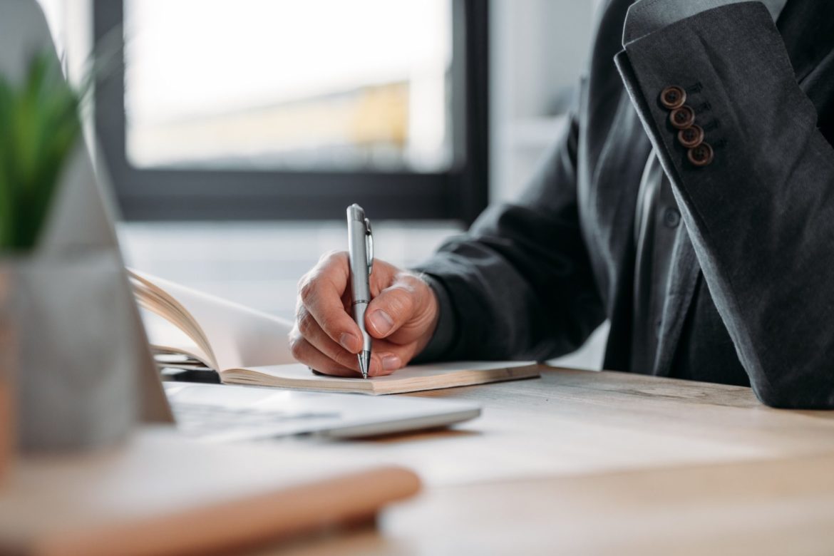 close-up partial view of businessman taking notes in notebook at workplace
