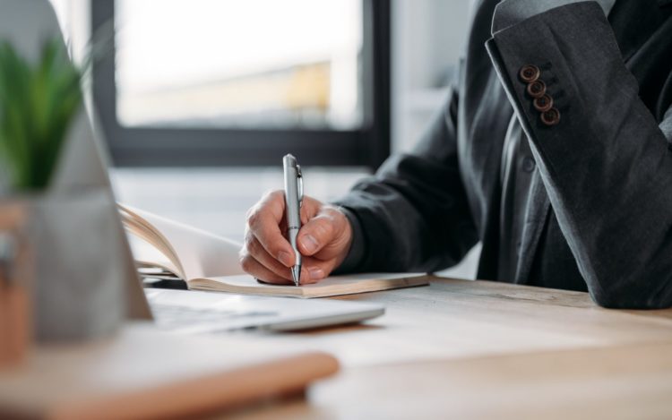 close-up partial view of businessman taking notes in notebook at workplace