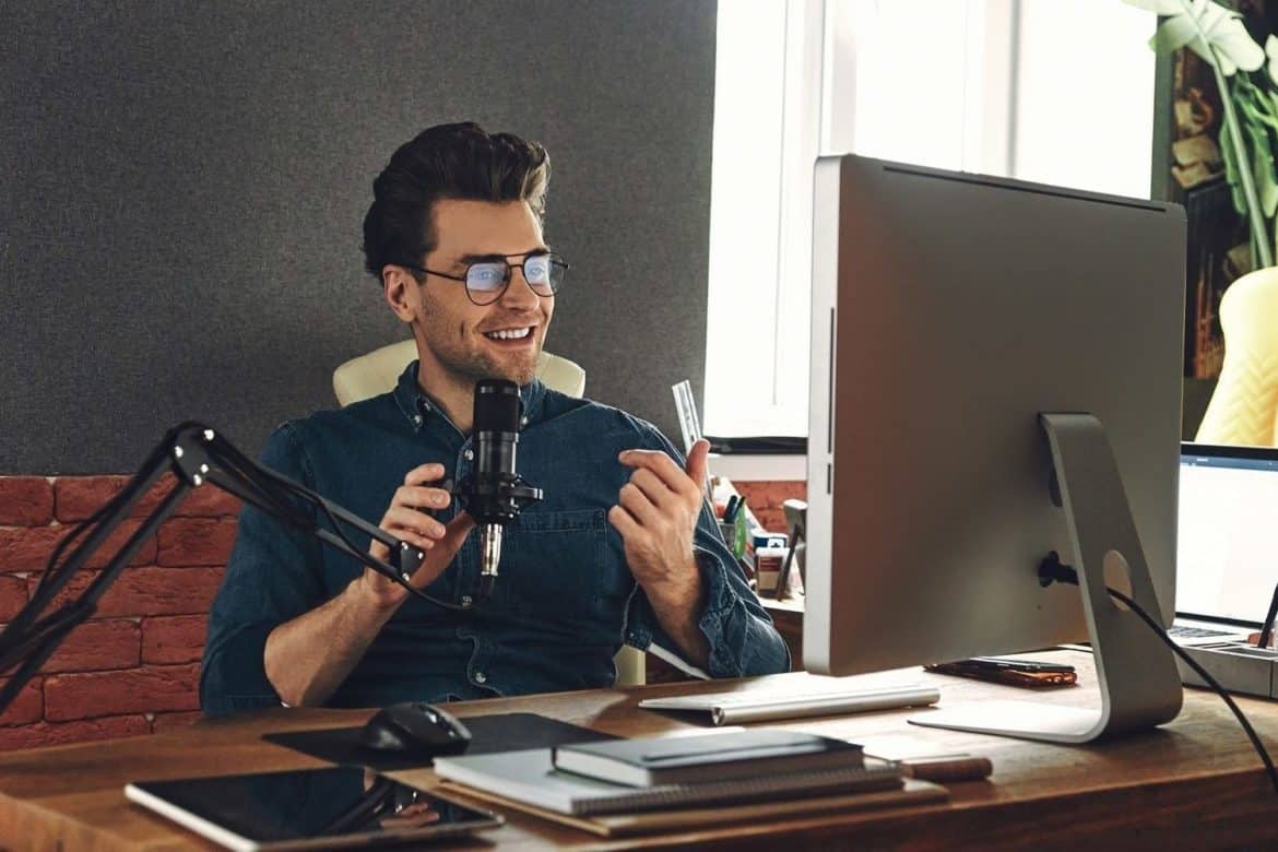 Handsome young man using microphone and gesturing while recording podcast in studio
