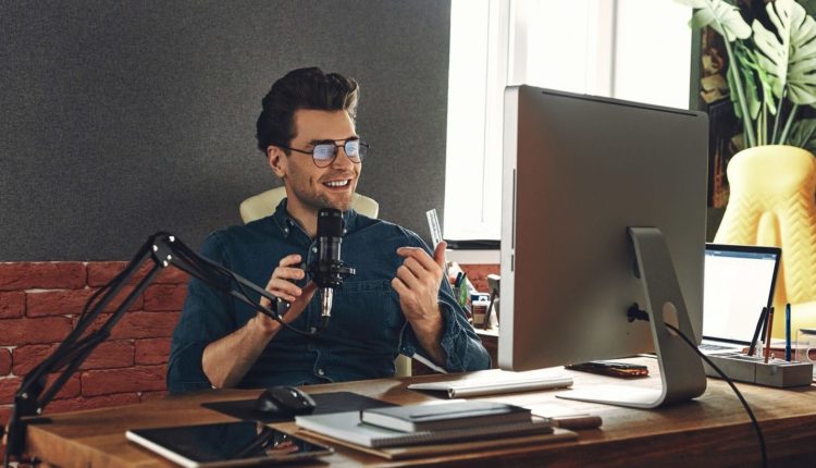 Handsome young man using microphone and gesturing while recording podcast in studio