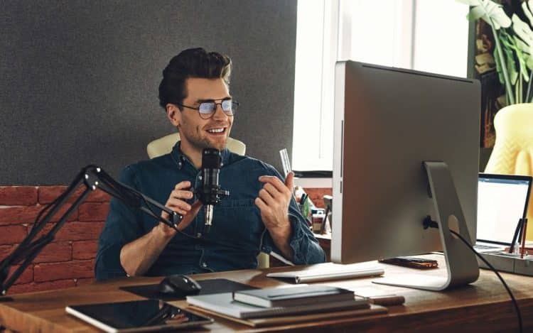 Handsome young man using microphone and gesturing while recording podcast in studio