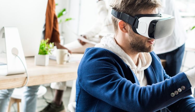panoramic shot of young businessman touching something with finger while using vr headset in office
