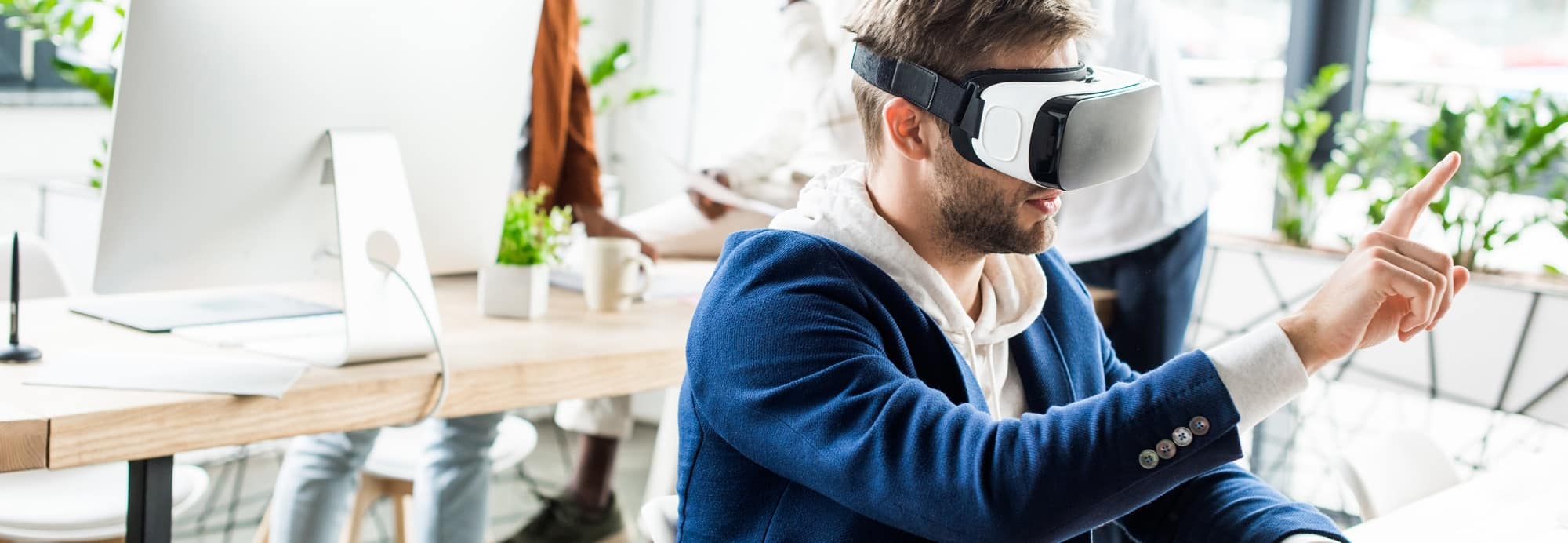 panoramic shot of young businessman touching something with finger while using vr headset in office