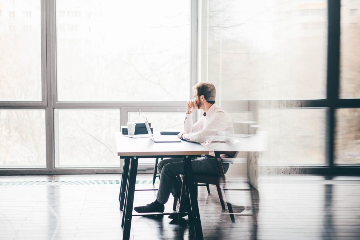 Young business man sitting at table looking at the window and thinking at modern office.