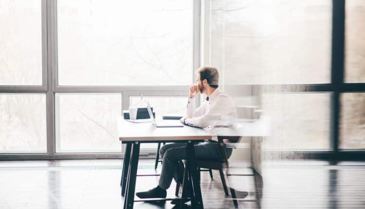 Young business man sitting at table looking at the window and thinking at modern office.