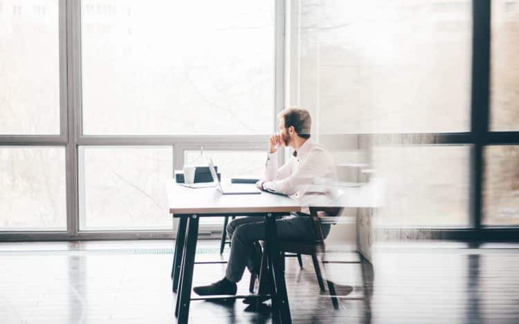 Young business man sitting at table looking at the window and thinking at modern office.