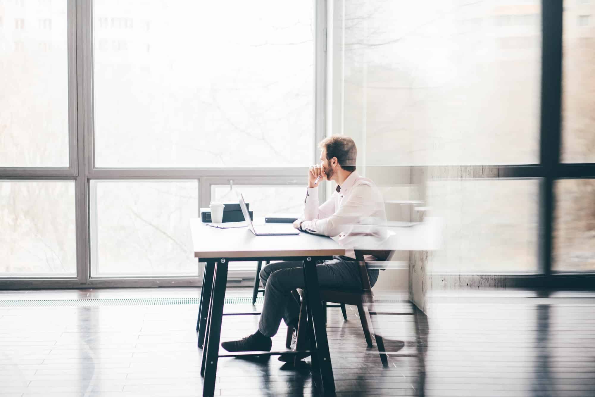 Young business man sitting at table looking at the window and thinking at modern office.